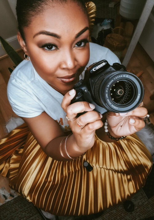 Light skinned Black woman poses on the floor with a Canon camera in her hand