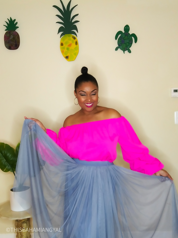 Black woman wears a pink off the-shoulder blouse with a flow skirt.