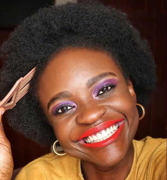 Image of dark skinned black woman with red lipstick smiling directly into the camera