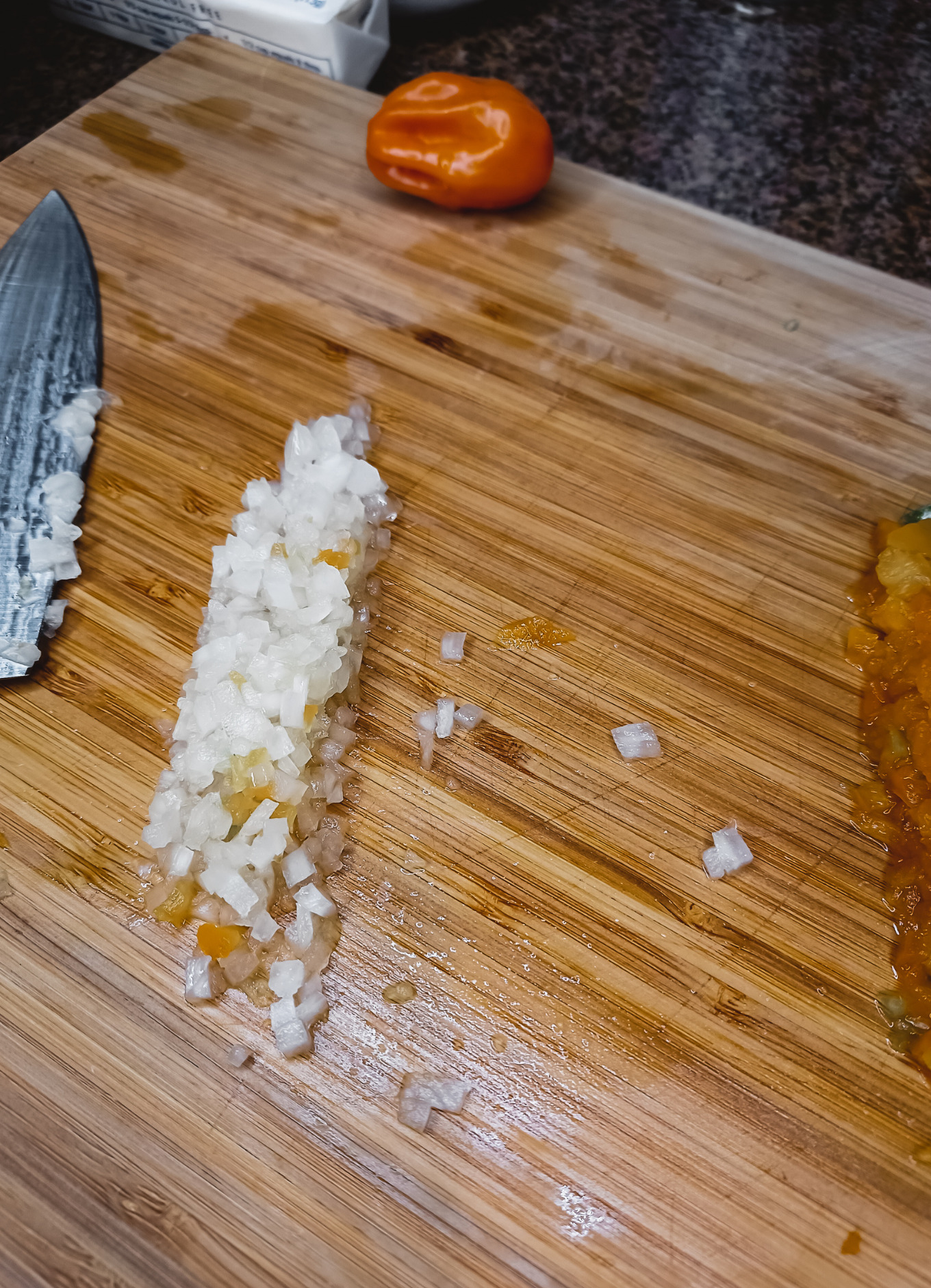 A cutting board with a knife, habanero pepper and onion.