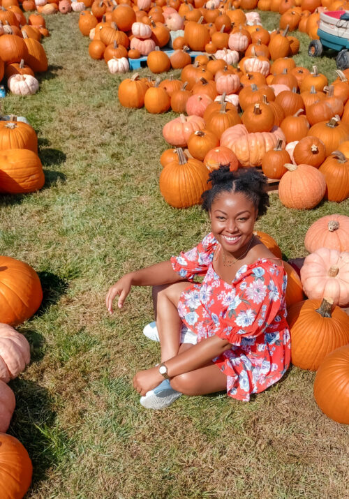 Light skinned black woman smiles and sits in the grass at a pumpkin patch in Alexandria Virginia This Bahamian Gyal