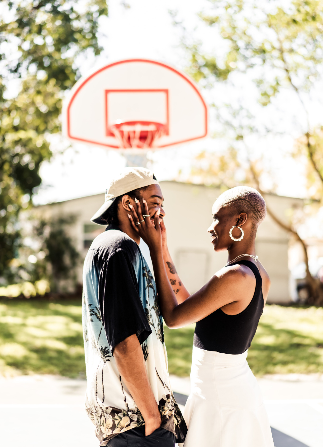A black woman holds a black man's face. The two of them are standing on a basketball court in their home's backyard
