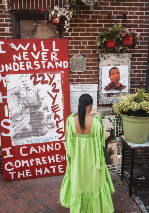This Bahamian Gyal blogger Rogan stands in front of a makeshift memorial for George Floyd in Fells Point, Baltimore. A sign that reads, "I will never understand" is shown in the background.