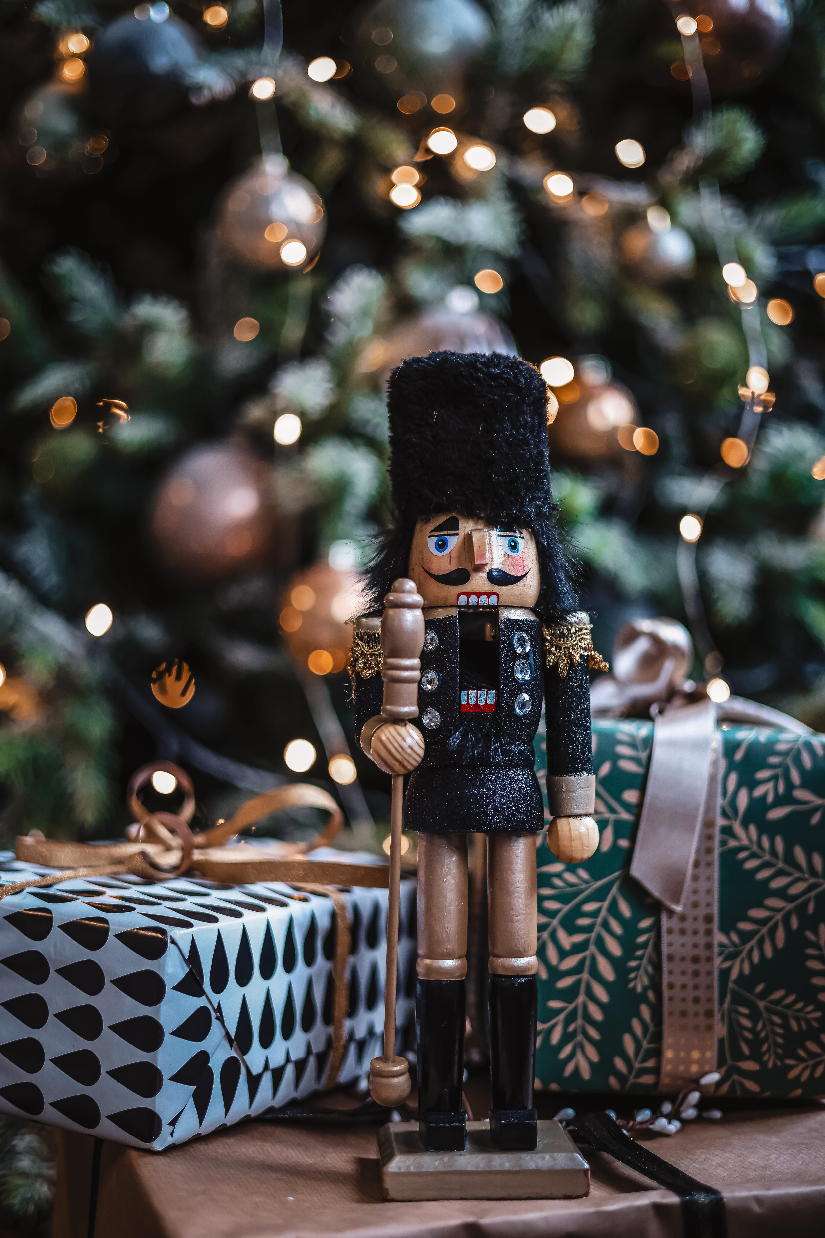 A nutcracker is placed in front of a beautiful illuminated Christmas tree with wrapped gifts. This year, I'm giving you 25 Christmas gift ideas everyone will love.