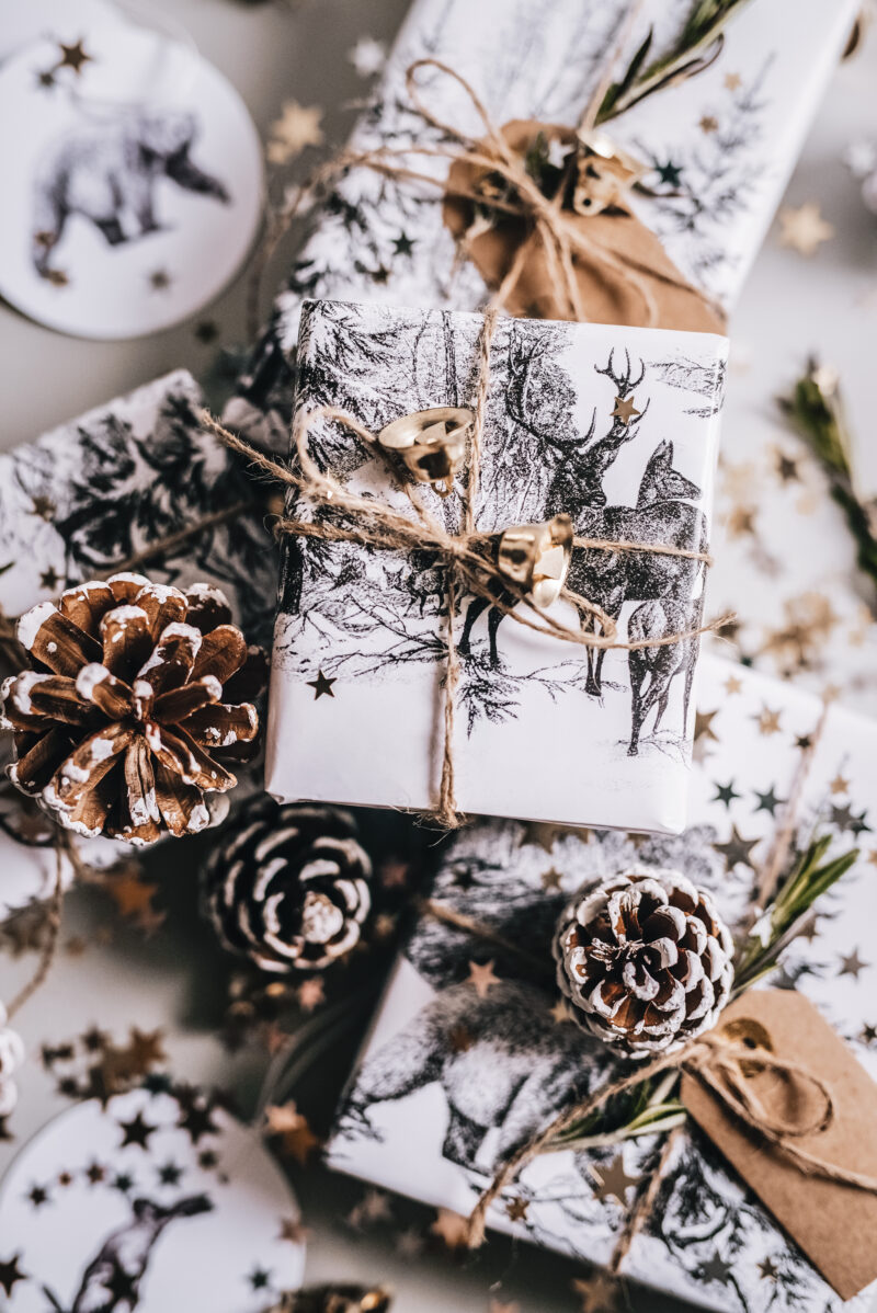 White Christmas gift boxes with deer wallpaper like on a table surrounded by pinecones.
