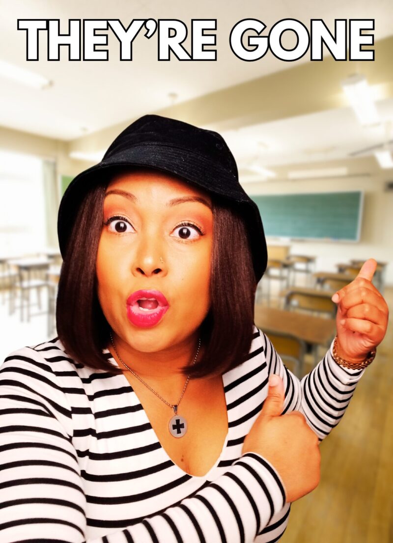 Blogger Rogan poses in front of an empty classroom. A chalkboard can be seen in the background. Rogan wears a black hat and a black and white striped shirt.
