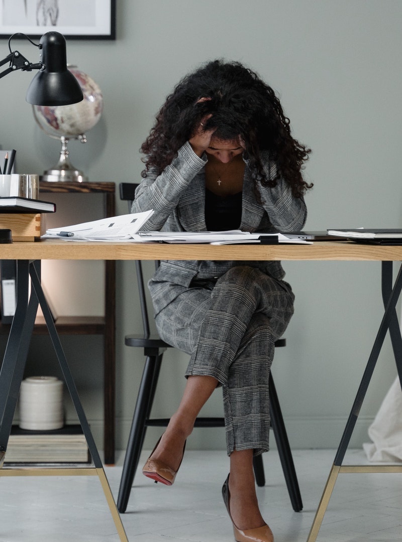 Black woman sits at desk with her head down disappointed about her abusive relationship with money