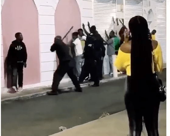 Royal Bahamas Police Force officers line a group of young men up against a wall and beat them with batons. 