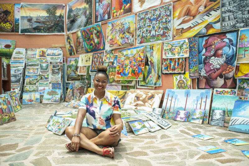 Bahamian Blogger, Rogan Smith is surrounded by local art in Downtown Nassau. The Bahamas will reopen for travel on July 1. 