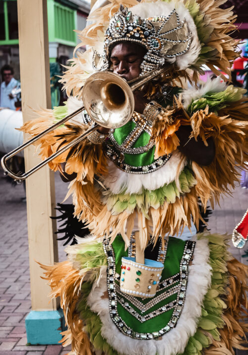 An image of a black Bahamian man in a traditionial junkanoo costume. He is shown blowing a horn.