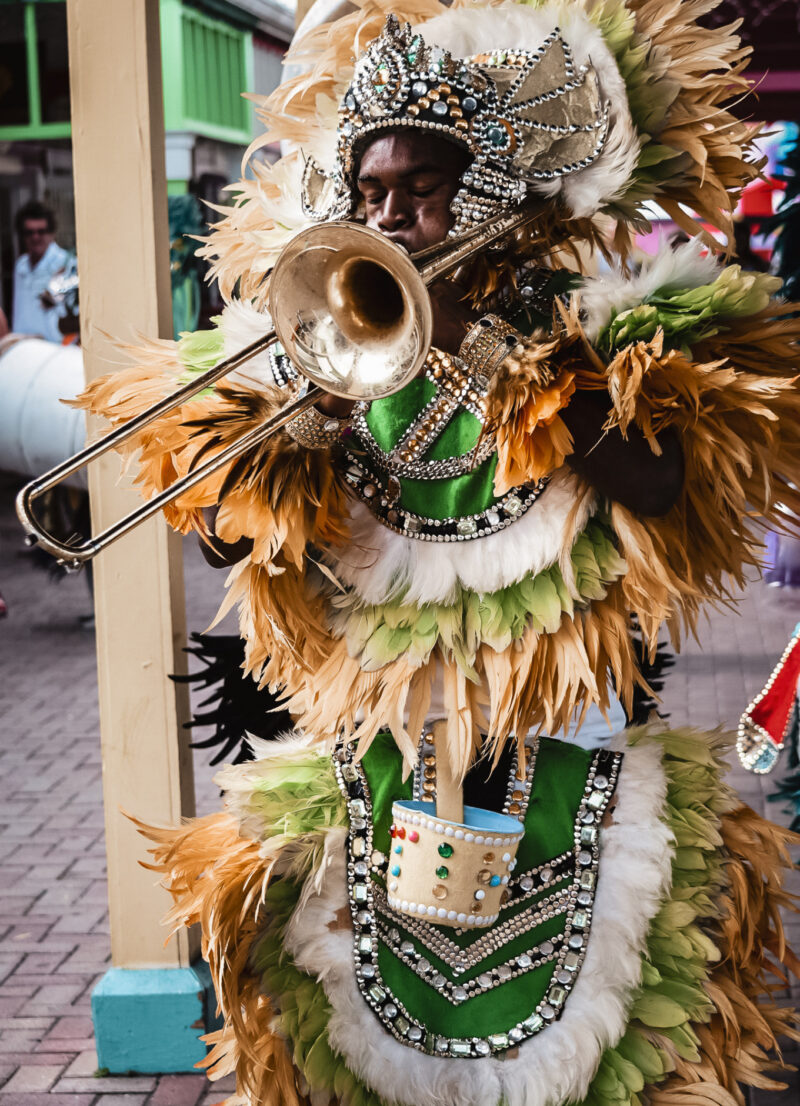 An image of a black Bahamian man in a traditionial junkanoo costume. He is shown blowing a horn.