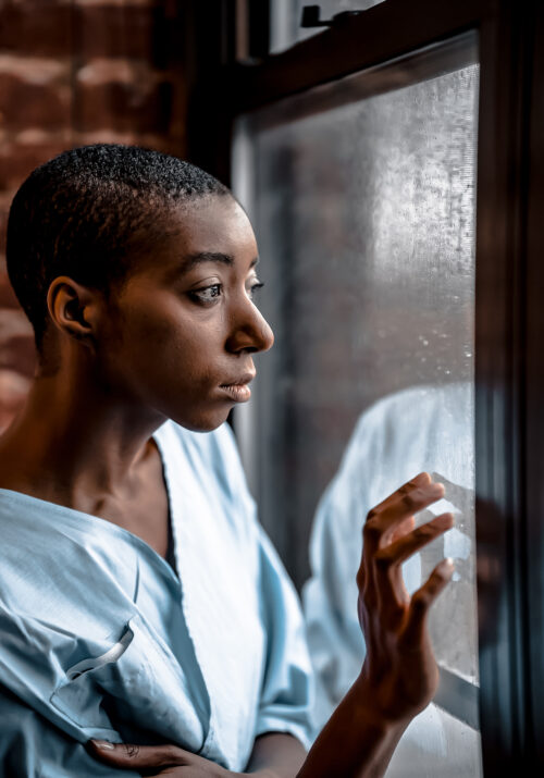 Black female hospital patient stares out of window photo by klaus nielsen