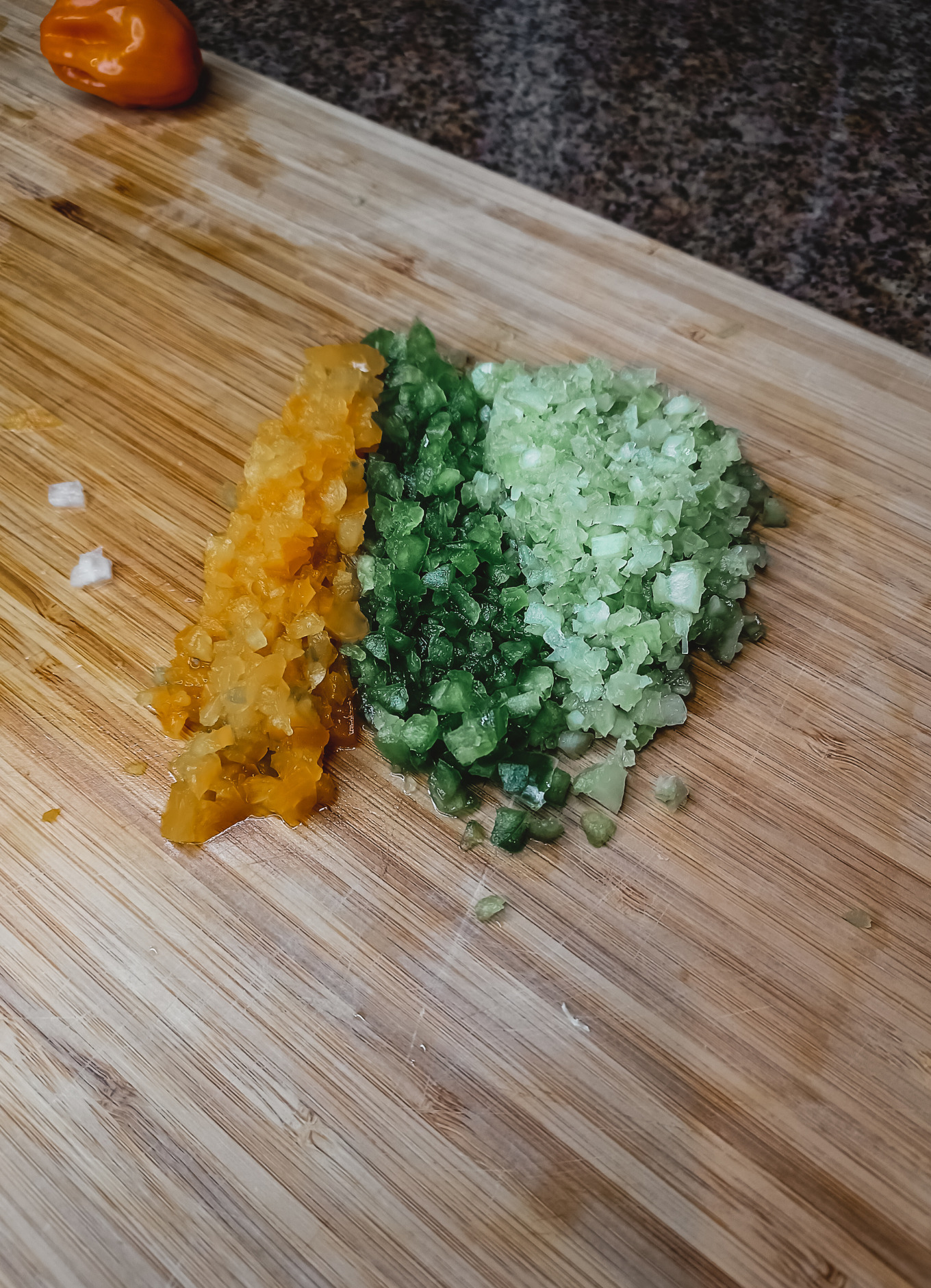 A cutting board with a habanero, yellow bell pepper, green pepper and celery