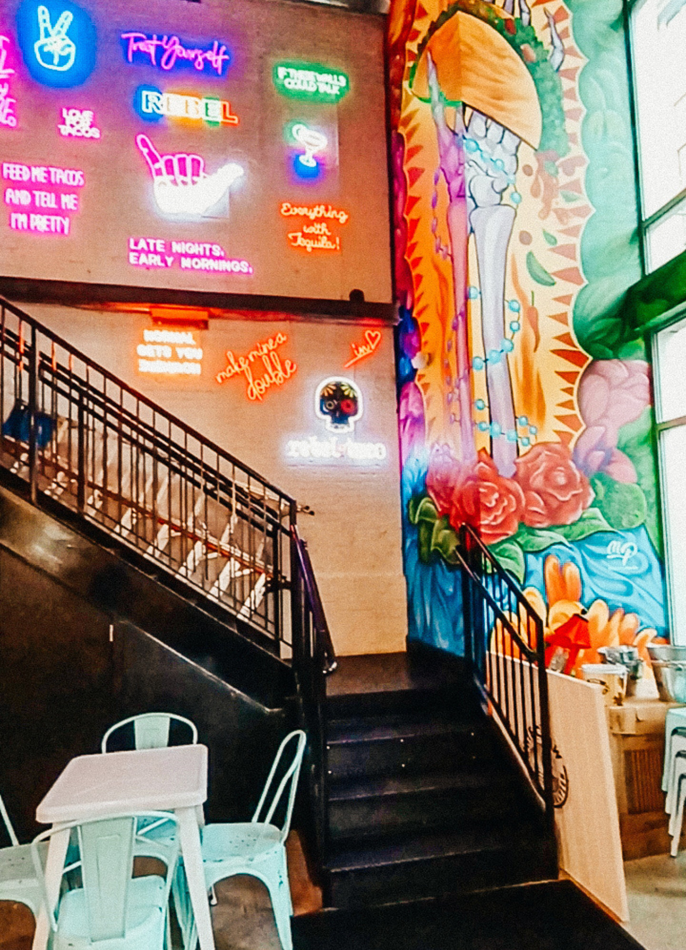 The colourful interior of Rebel Taco restaurant in Washington, DC. Neon signs adorn the wall all the way to the high ceilings.