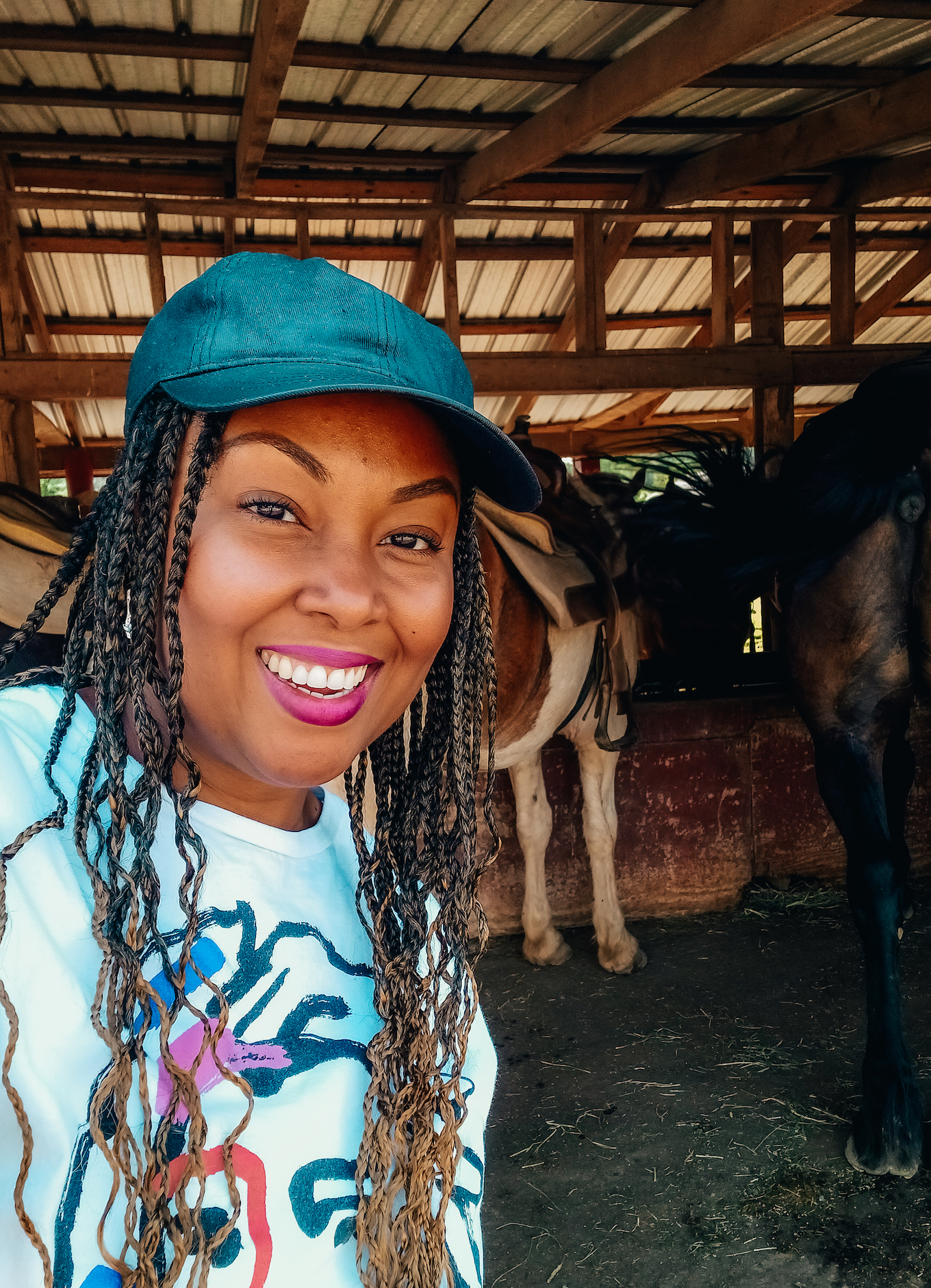 A young black woman smiles at the camera with a row of horses in the background.