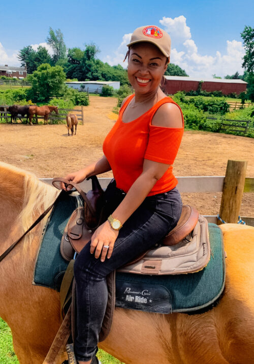 This Bahamian Gyal blogger Rogan sits on top of a horse at Piscataway Riding Stable. She is smiling and holding the reins in her hand.