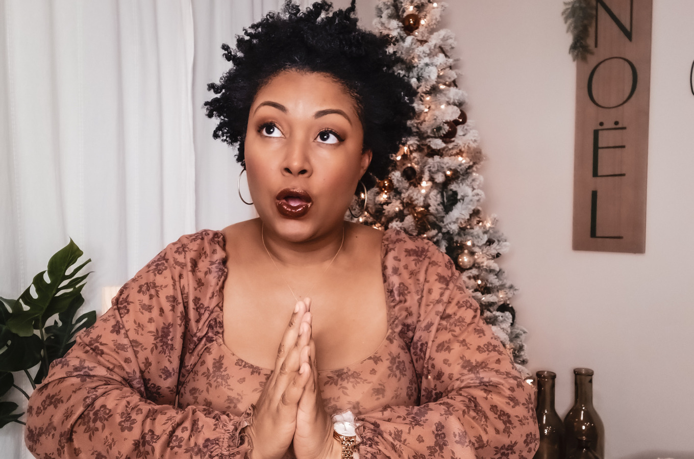 A light skinned black girl with natural curly hair sits in front of a Christmas tree with her hands in the prayer stance
