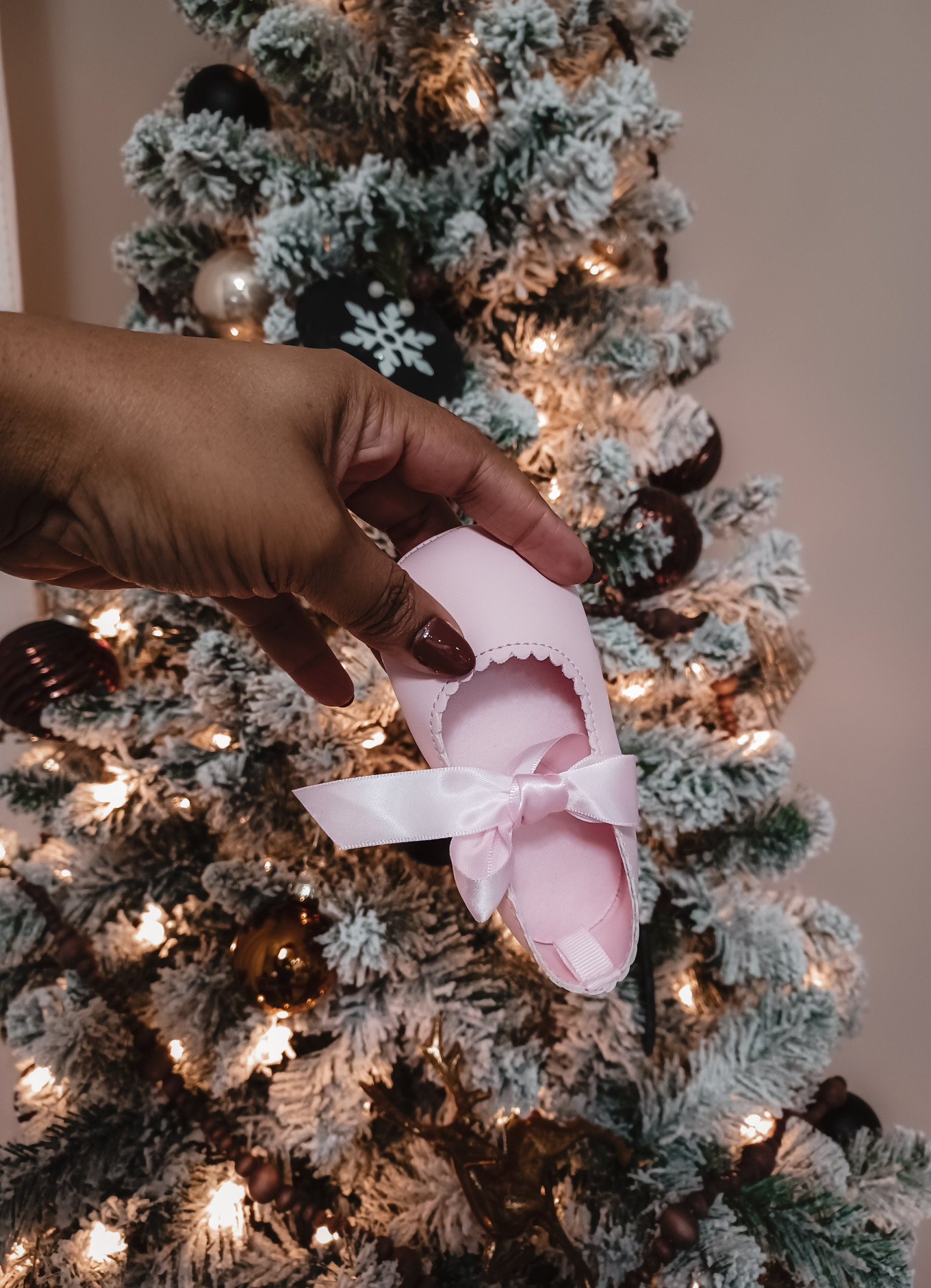 A pink baby bootie is shown in front of a Christmas tree