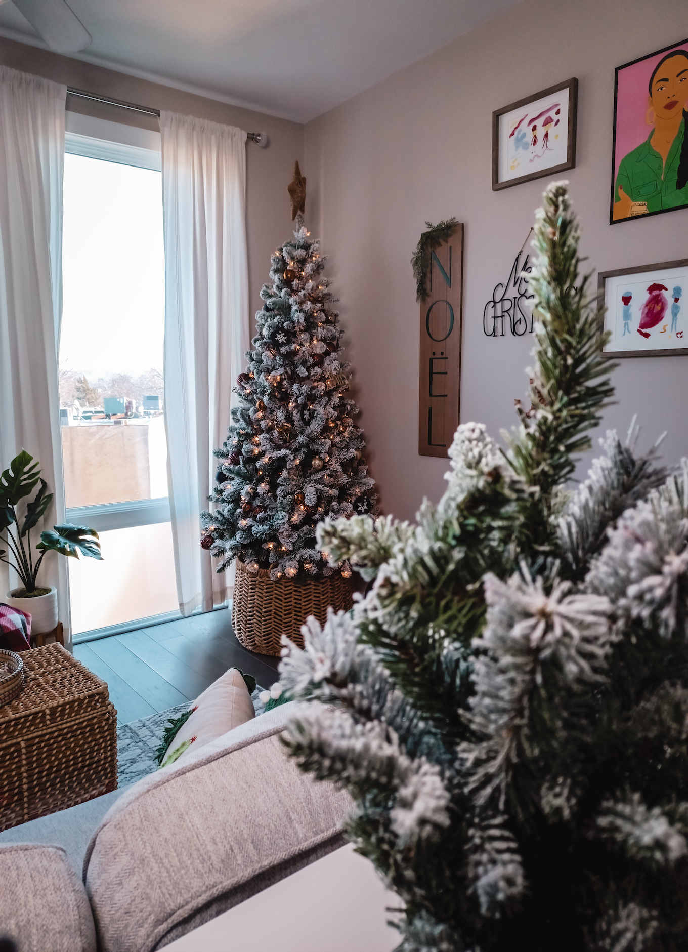 Photo shows a flocked Christmas tree in the distance in a living room. Adding holiday decor is a quick way to make a small apartment feel Christmasy.