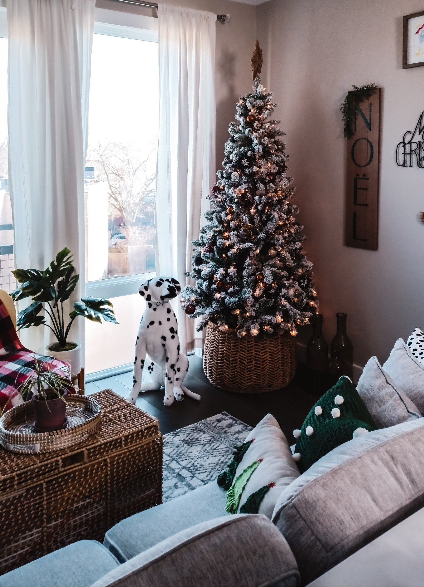 A surefire way to make a small apartment feel Christmasy is to add tiny, but memorable holiday accents to the space. This photo features plants, green throw pillows, a stuffed Dalmatian dog and a gorgeous lit Christmas tree with gold, bronze, black and cream-coloured decorations.