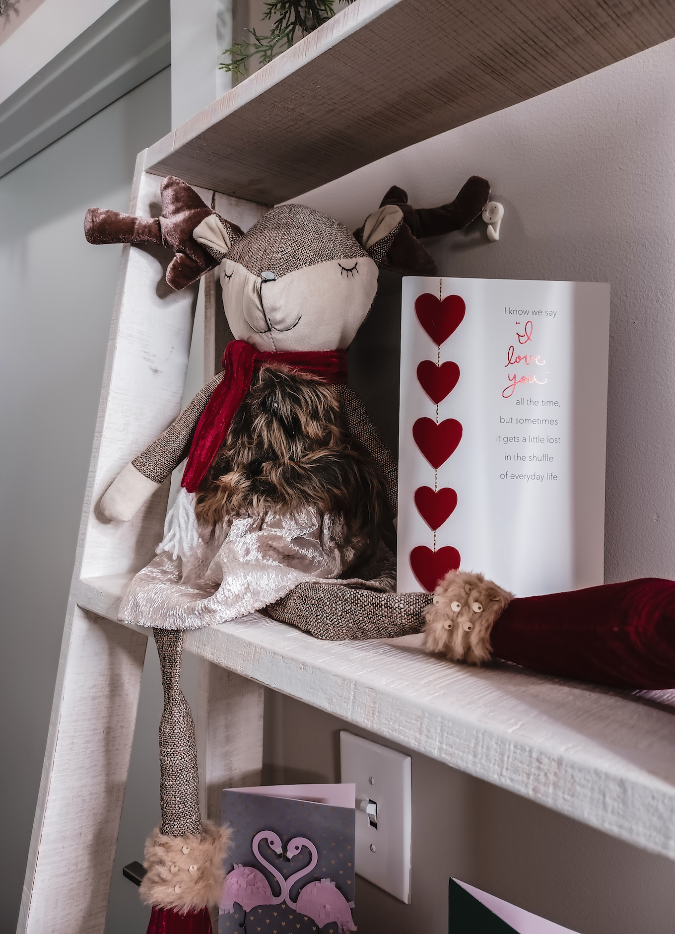 A smiling plush reindeer with a red scarf sits on a shelf