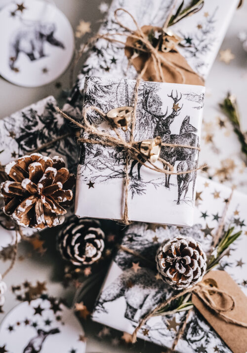 White Christmas gift boxes with deer wallpaper like on a table surrounded by pinecones.