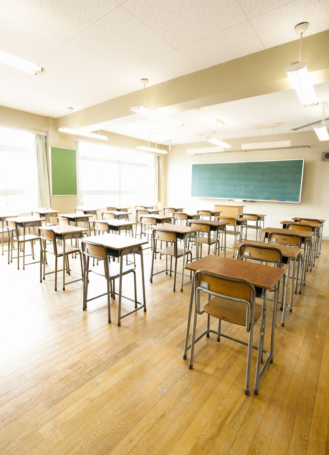 Photo shows an empty classroom with a chalkboard in the background and empty desks and chairs in the foreground.