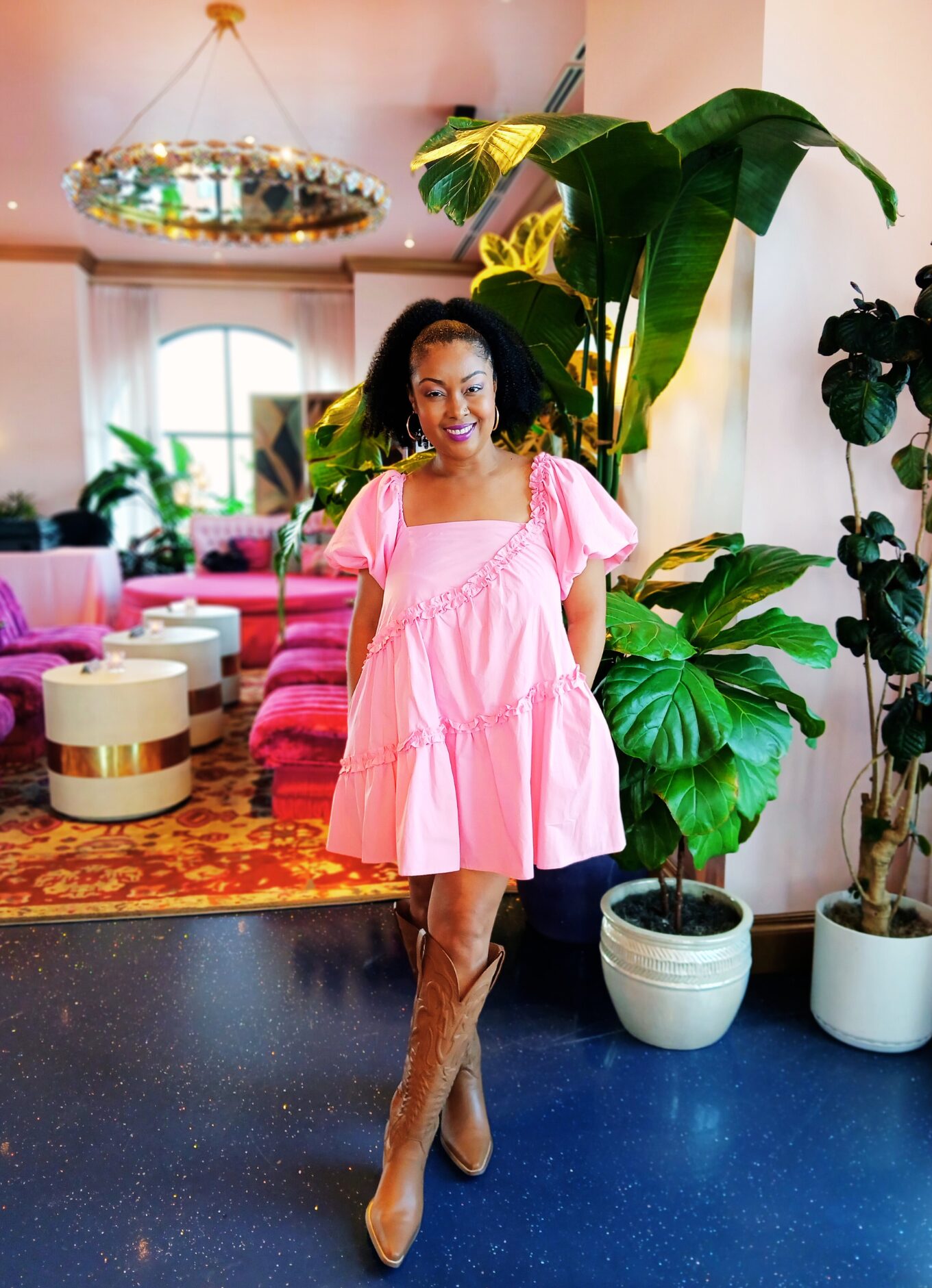 Blogger Rogan poses and smiles inside of the cocktail bar, White Limozeen. She is wearing a short, tiered pink dress with brown leather cowboy boots