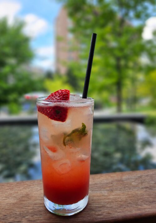 Image of a frosty glass with a strawberry drink inside. The glass is in the foreground while a blurred pool is shown in the background.