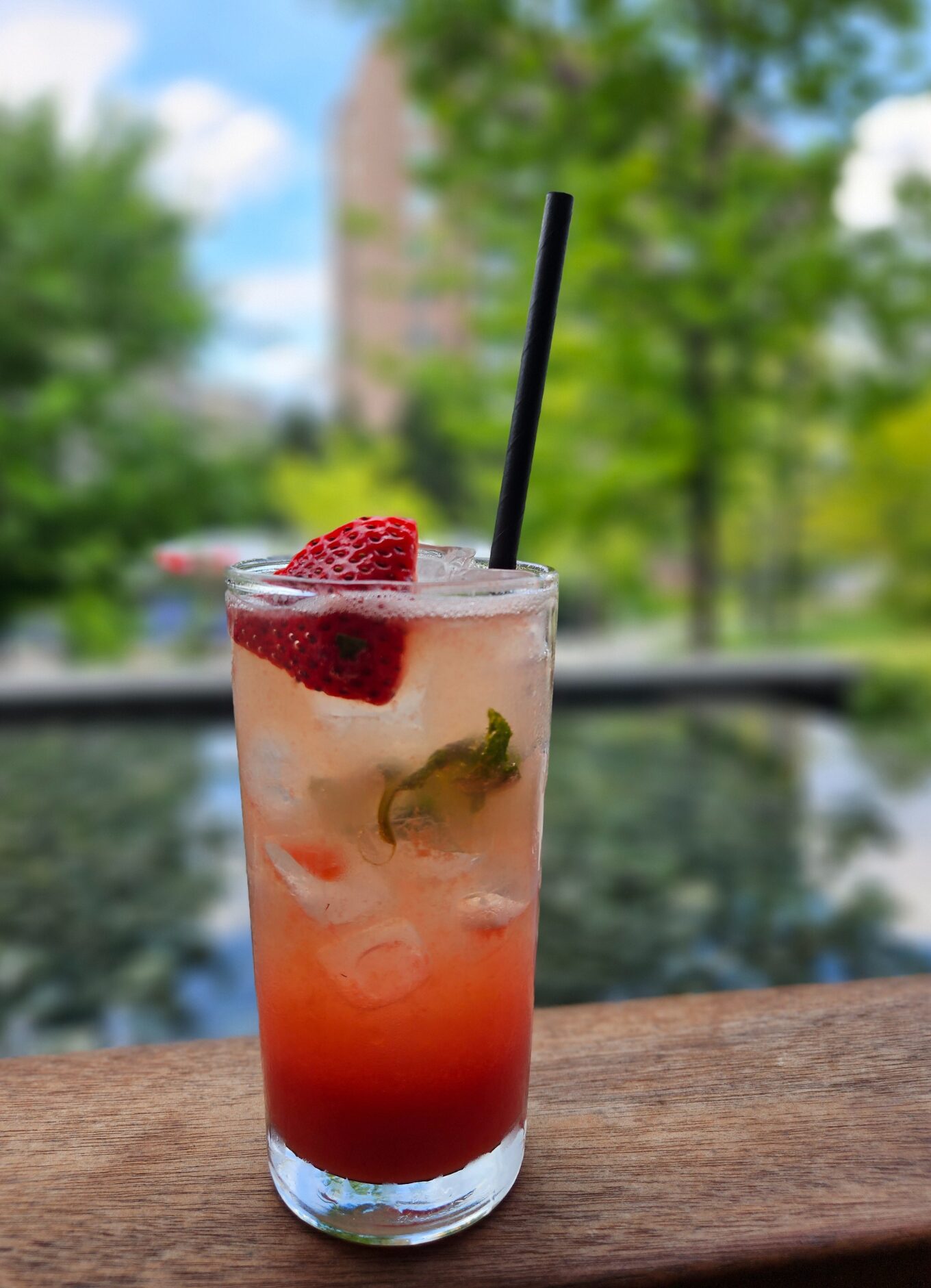 Image of a frosty glass with a strawberry drink inside. The glass is in the foreground while a blurred pool is shown in the background.