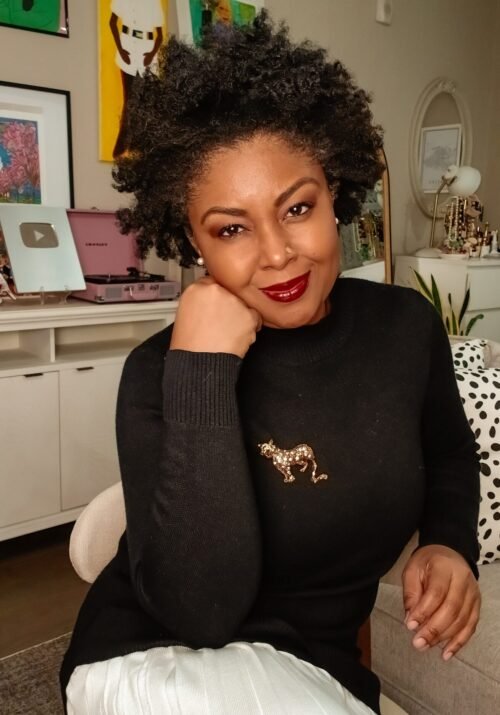 How To Cultivate Gratitude On Thanksgiving - This Bahamian Gyal blogger, Rogan sits in her living room. She is sporting a curly afro, a black sweater, a pleated cream skirt and a jaguar pin