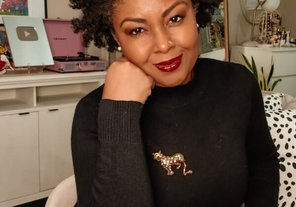 How To Cultivate Gratitude On Thanksgiving - This Bahamian Gyal blogger, Rogan sits in her living room. She is sporting a curly afro, a black sweater, a pleated cream skirt and a jaguar pin