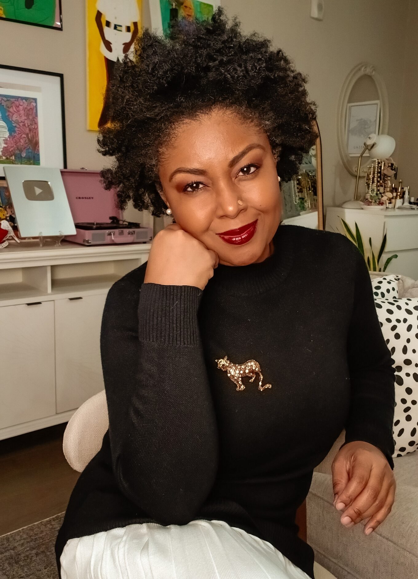 How To Cultivate Gratitude On Thanksgiving - This Bahamian Gyal blogger, Rogan sits in her living room. She is sporting a curly afro, a black sweater, a pleated cream skirt and a jaguar pin