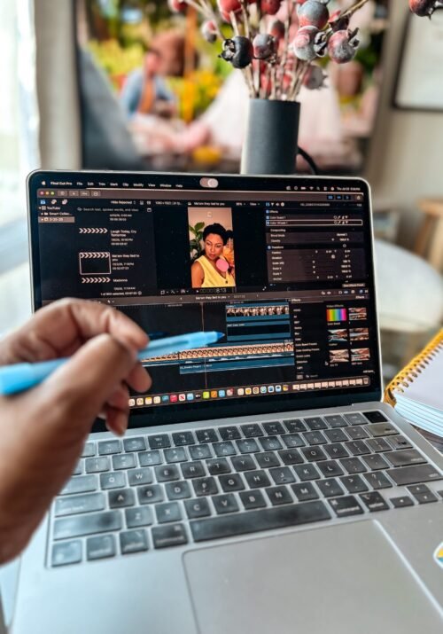 Creator workspace with a laptop displaying a YouTube Shorts editing timeline, alongside a notepad and flowers
