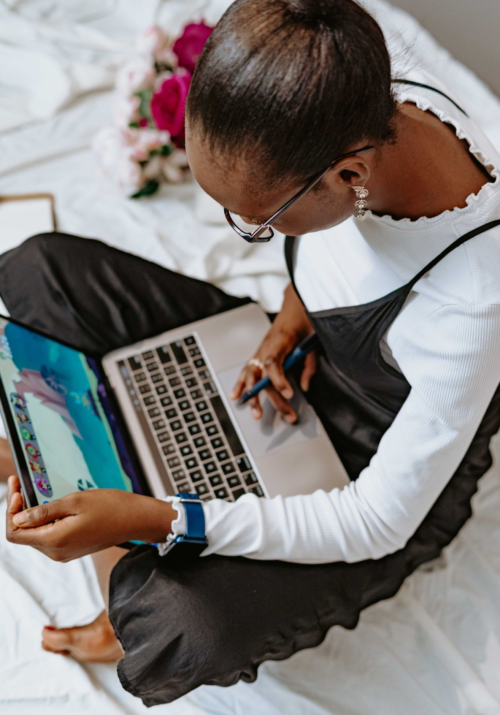An African American woman sits on a bed with her Apple laptop in hand, reading an email about a YouTube sponsorship scam.